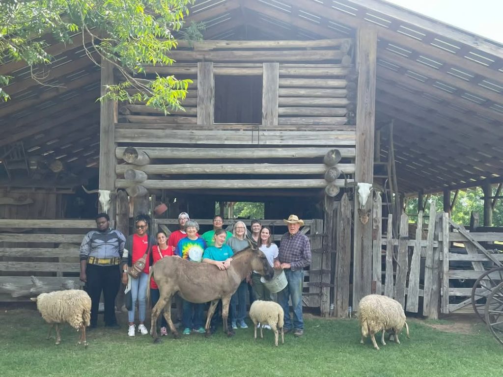 Pathway Weavers pose with lambs in front of barn