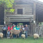 Pathway Weavers pose with lambs in front of barn