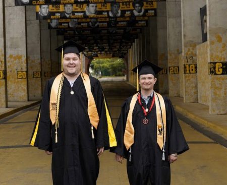 RISE graduates Taylor Carley, left, and Dan Lewis, right, pose in their cap and gown at the Eagle Walk on campus.