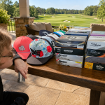 Natalie squatted next to a table full of donated golf balls and hats.