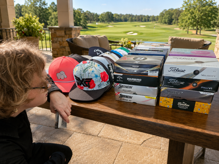 Natalie squatted next to a table full of donated golf balls and hats.